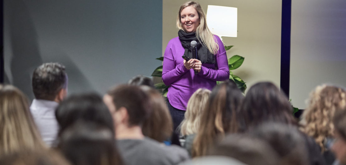 Holly stands in front of audience as part of her talk on the inescapable competency trap women face at work